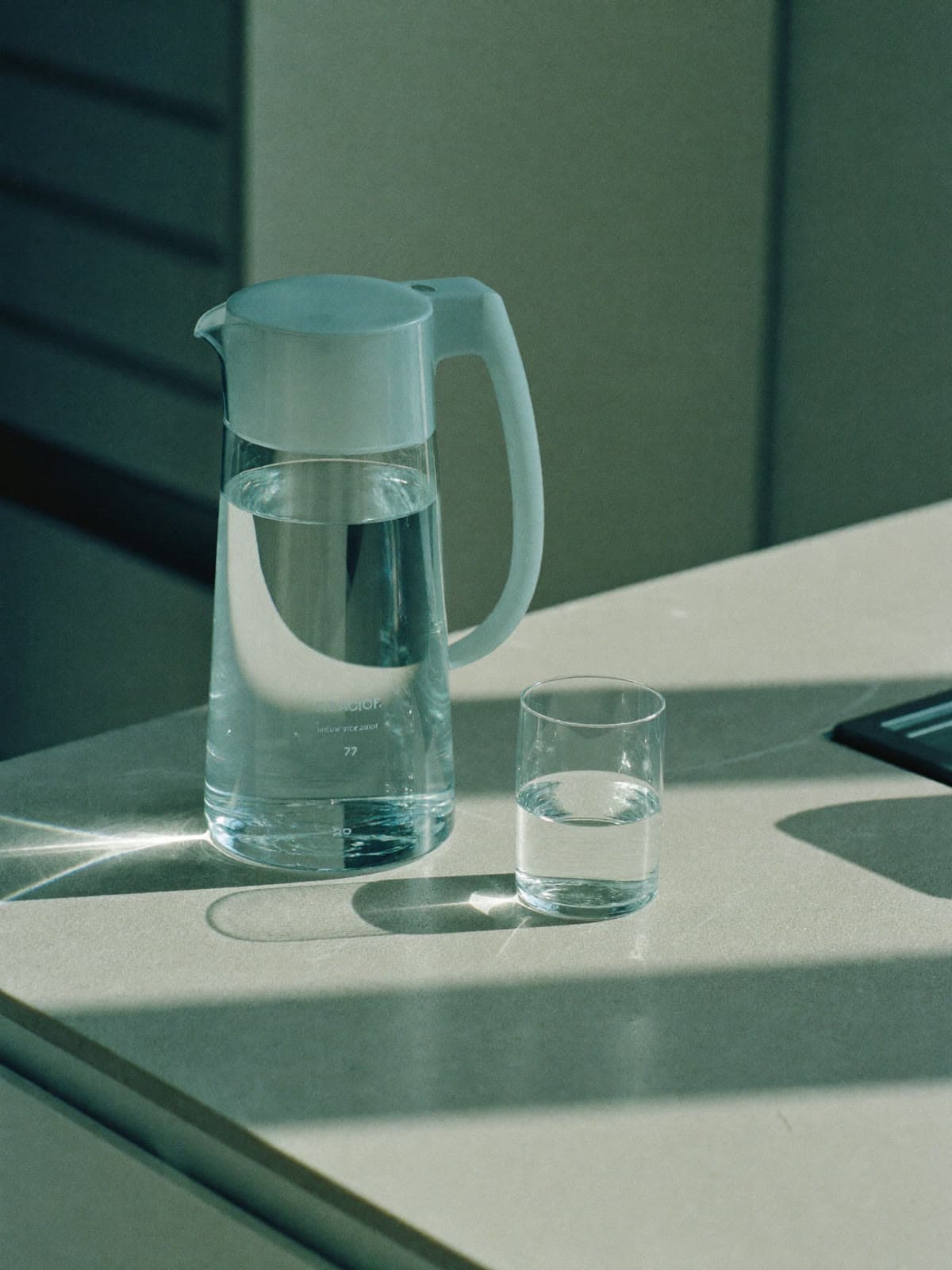 Clear water pitcher and filled glass on a pale stone kitchen counter in morning light