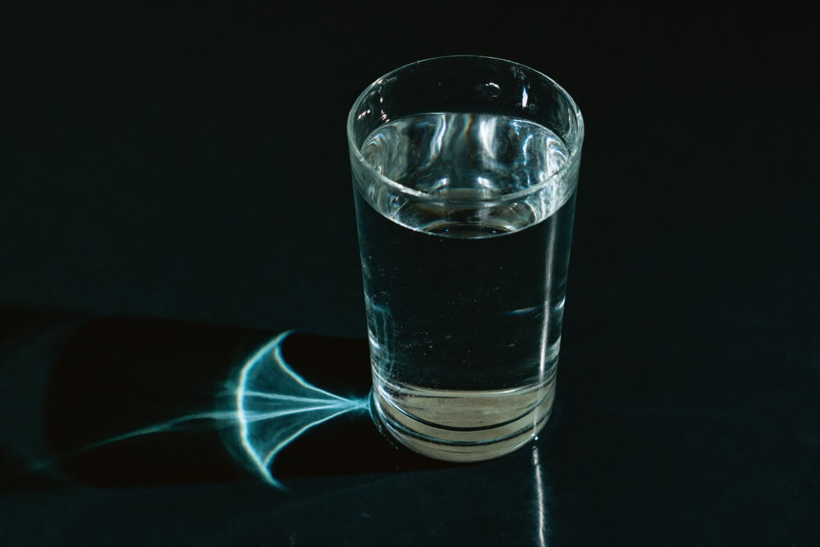 A tall glass of water on dark stone with caustic light patterns